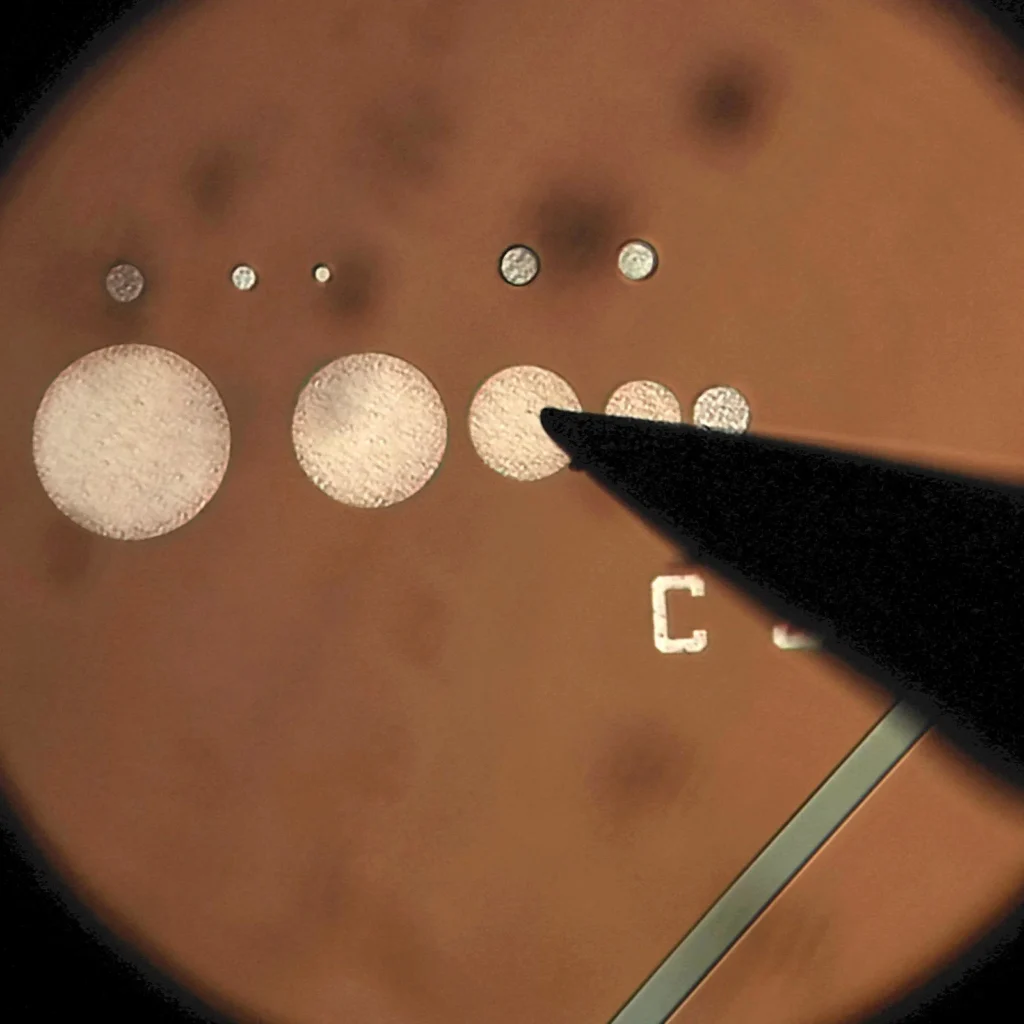 Close-up view of semiconductor test structure with probe needle contacting patterned circular test pads for electrical measurement