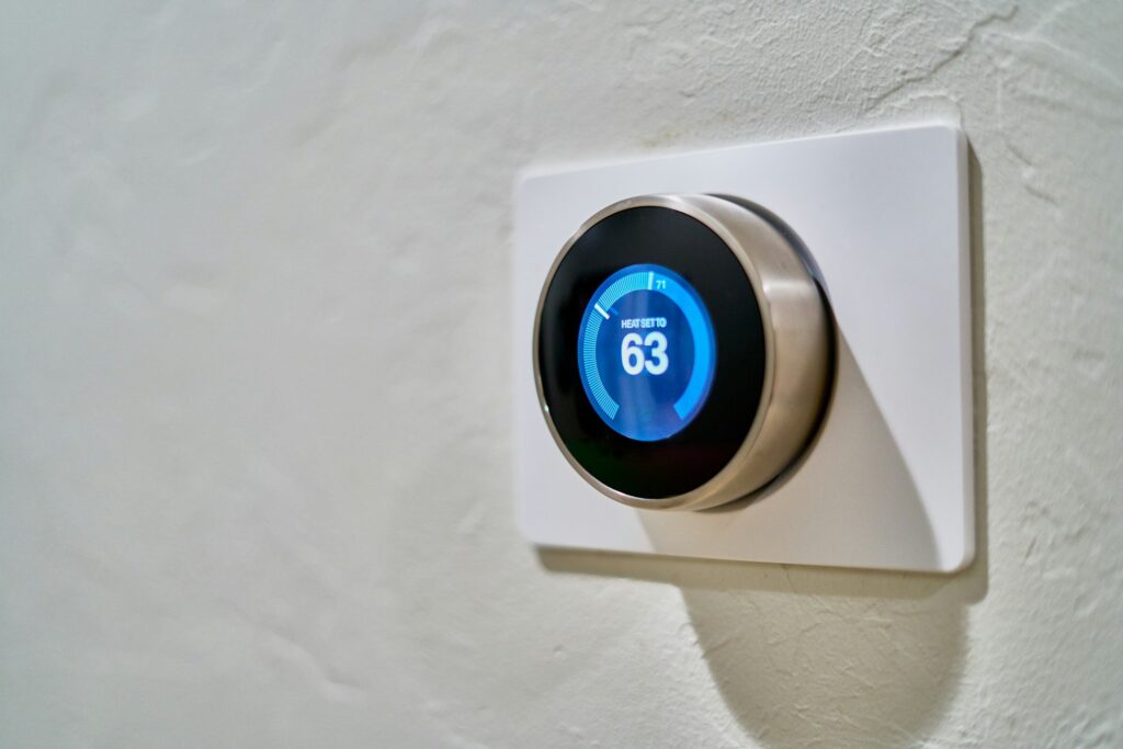 Smart thermostat mounted on wall displaying a temperature setting of 63 degrees for automated home climate control